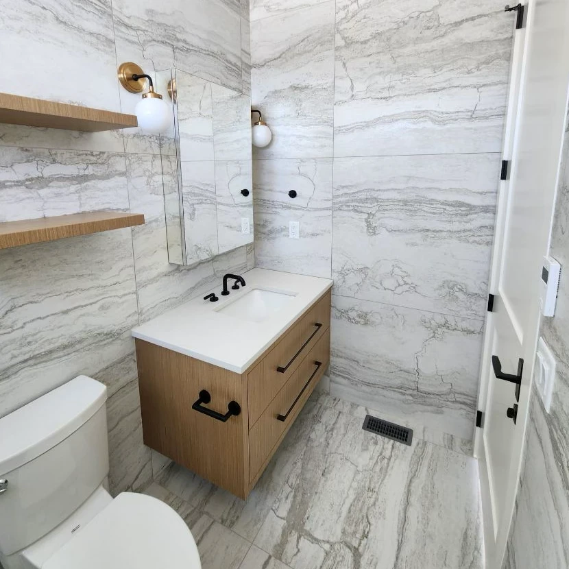 A contemporary bathroom renovated by Nailed It Developments Inc. featuring marble tiles and wooden vanity in Kelowna.